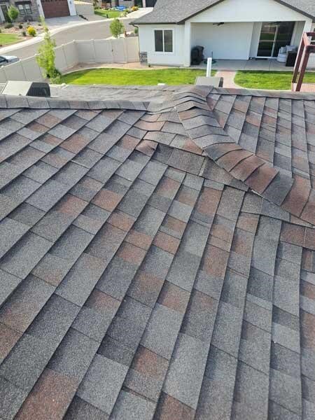 Severe roof damage featuring buckled asphalt shingles in need of professional repair.