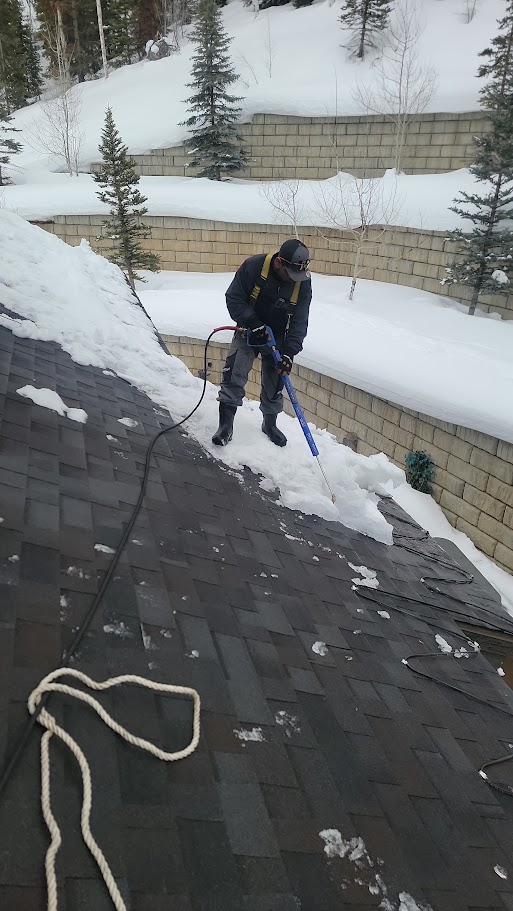 Worker clearing snow from a shingle roof.