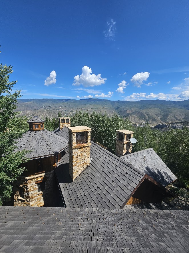 Custom residential roof replacement with grey shingles and stone chimneys on a luxury mountain home.